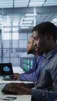 Vertical Cheerful server room workers laughing together in office while ensuring minimal downtime. Jolly engineers having fun in data center, using data analytics to monitor performance, camera A video