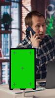 Chroma key tablet next to freelancer in home office sitting at desk in front of laptop, answering phone call. Isolated screen device next to freelancer receiving telephone call on smartphone, camera A video