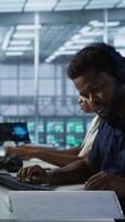 Vertical Engineer in server room looking over documents, developing disaster recovery plans ensuring minimal downtime. Worker reading paperwork in data center, using analytics to monitor performance, camera A video
