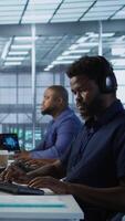 Vertical Data center admin typing on keyboard, maintaining company network infrastructure by configuring hardware. African american worker in server hub ensuring optimal system performance, camera A video