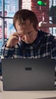 Stressed man in home office scratching head with pen, upset after having to answer too many emails on laptop. Fatigued teleworker feeling overworked by too many project tasks, camera A video