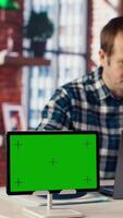 Green screen tablet next to employee completing spreadsheets on laptop and listening music. Chroma key device next to worker in home office wearing headphones editing documents, camera B video