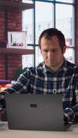 Worker listening music, analyzing data on laptop at desk, compiling analytical reports. Employee wearing headphones, using notebook device, writing down information, camera A video