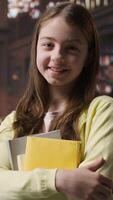 Vertical Portrait of sweet preadolescent carrying her books and class notes in the library, preparing for an intense studying session with her textbooks. Academic environment to ensure development. Camera A. video