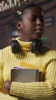 Vertical Portrait of african american scholar arriving at the library with her learning materials and books, holding textbooks with class notes to the study area. Pupil studying to pass her exams. Camera A. video