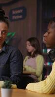 Vertical Caucasian tutor guiding elementary school girl at a library desk, providing private lessons to aid in their academic development with work books and notes. Teacher discussing with scholar. Camera B. video