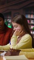 Vertical African american professor mentoring diverse students in the library, learning in an academic library filled with curriculum books. Woman tutoring her class pupils on literature subject. Camera B. video