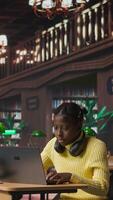 Vertical African american schoolgirl writing class notes on laptop in a library, working on a project with online information at a study desk. Pupil preparing for lessons at the academic institute. Camera B. video