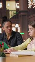 Vertical Female tutor mentoring schoolgirls in a school library setting, boosting their understanding of a subject through personalized guidance. Teacher doing private lessons with two pupils. Camera A. video