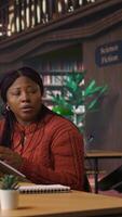 Vertical Black tutor mentoring schoolgirl in a school library study desk, boosting her understanding of a subject through personalized guidance. Professor hosts private lessons with pupil. Camera A. video
