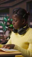 Vertical Black preteen pupil underlining key words and phrases for the learning session at the library, creating a summary to retain information easier. Focused scholar studying. Camera A. video