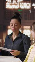 Vertical Female mentor providing instruction to diverse pupils during private lessons at the library, assisting with homework and school projects in the study area. Tutoring session for guidance. Camera A. video
