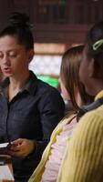 Vertical Female mentor providing instruction to diverse pupils during private lessons at the library, assisting with homework and school projects in the study area. Tutoring session for guidance. Camera B. video