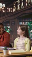 Vertical Diverse teen girls working with a tutor to complete class notes in a library, helps with learning and tutoring for the school subjects. Professor ensures diversity and child development. Camera A. video