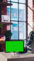 Green screen tablet next to employee completing spreadsheets on laptop and listening music. Chroma key device next to worker in home office wearing headphones editing documents, camera A video
