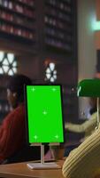 Vertical African american schoolgirl writing class notes next to chroma key in a library, working on a school project with online information on tablet. Pupil prepares for lessons and courses. Camera A. video