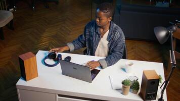 Woman arriving in apartment office, sitting down at desk, opening laptop to begin doing tasks. Teleworker starting job shift at home, preparing notebook device, logging in online, camera B video