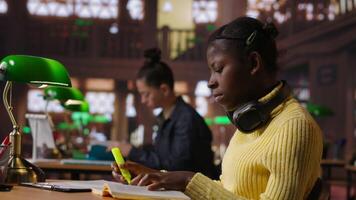Black preteen pupil underlining key words and phrases for the learning session at the library, creating a summary to retain information easier. Focused scholar studying. Camera B. video