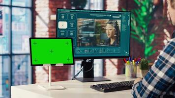 Man in home office uses AI program turning text prompt into videos next to isolated screen tablet. Person using text to generative models on computer and chroma key device, camera B