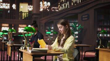 Young teen girl engrossed in reading books at the school library, focusing on literature and knowledge while she is preparing for her academic lessons and other class assignments. Camera A. video