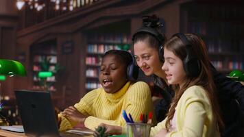 Young students and tutor attending an online class via call in the library, focused on distance learning and completing a school assignment with other classmates on the network. Camera B. video