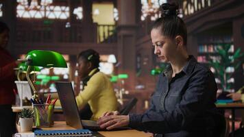 porträtt av en självsäker bibliotekarie arbetssätt på henne bärbar dator i en offentlig bibliotek, tillhandahålla akademisk Resurser och vägledning. specialist utvärdera inlärning material inom de databas. kamera a. video
