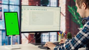 Software engineer at computer coding, creating software using isolated screen tablet. IT specialist in home office working with code editor, building applications using PC and mockup device, camera B video