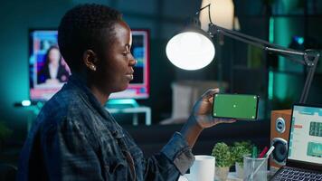 Self employed woman at home checks statistics on laptop while using chroma key smartphone. Remote worker holding isolated screen phone in landscape mode, analyzing business graphics video
