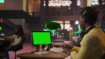 African american pupil immersed in essay writing next to copy space display at a library desk, completing homework school assignments and demonstrating academic skills. Camera A. video