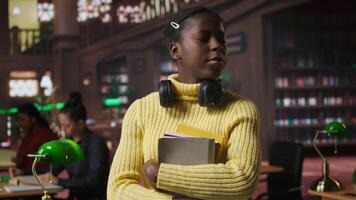 Portrait of african american scholar arriving at the library with her learning materials and books, holding textbooks with class notes to the study area. Pupil studying to pass her exams. Camera A. video