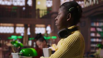 Portrait of african american scholar arriving at the library with her learning materials and books, holding textbooks with class notes to the study area. Pupil studying to pass her exams. Camera B. video