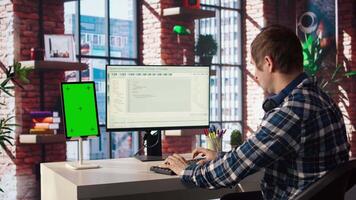 Programmer at desk typing code into computer, developing software programs, consulting green screen tablet. Man in home office fixing errors in application using chroma key device and PC, camera A video