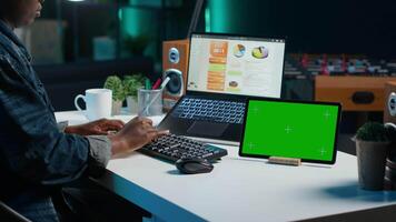 Entrepreneur working from home, using green screen device to write notes. Remote worker in personal apartment office using laptop, transcribing important info on mockup tablet video