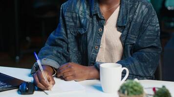 Entrepreneur working at home office desk on laptop, browsing the internet and writing in notebook. Woman using pen, notepad and digital device while teleworking, camera A video