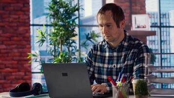 Freelancer in home office sitting at desk in front of laptop, answering phone call. Remote employee using notebook to do job online, receiving telephone call on smartphone, camera B video