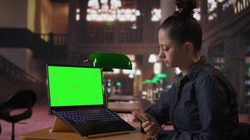 Professional librarian working on her laptop next to mockup screen in a public library, providing academic resources and guidance. Evaluating educational information within the database. Camera A. video