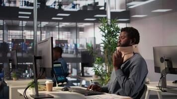 Black general manager suffering from a neck injury wears cervical foam, struggling with an uncomfortable position at his desk. Analyst trying to solve his daily tasks but being in pain. Camera B. video