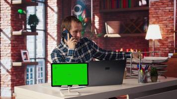 Green screen tablet next to man using laptop, answering phone call while checking emails displayed on screen. Mockup device next to worker in telephone call with friend at work, camera A video