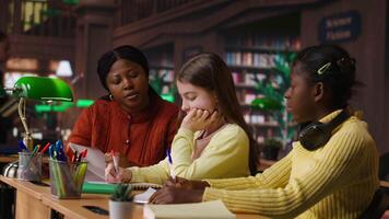 African american professor mentoring diverse students in the library, learning in an academic library filled with curriculum books. Woman tutoring her class pupils on literature subject. Camera B. video