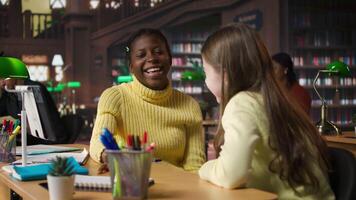 Happy two girls emphasizing their friendship with an embrace at the library, taking a break from study session and chatting about something. Classmates and friends having fun together. Camera A. video