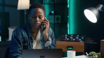 Woman receiving phone call from friend while working from home on laptop in personal office. Freelancer speaking with mate online using cellphone while solving tasks, camera A video
