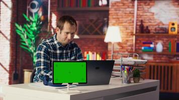 Mockup tablet next to worker listening music, analyzing data on laptop at desk, compiling reports. Isolated screen device next to employee putting headphones on, using notebook device, camera B video