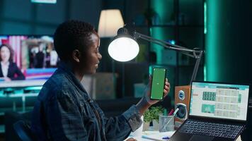 Teleworker in home office checks statistics on laptop, crosschecking with data on green screen smartphone. Person holding mockup mobile phone, analyzing company revenue numbers video