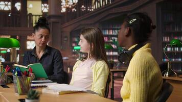 Elementary students receiving support from a tutor working on homework assignments in a diverse learning environment in the school library. Professor guiding her pupils before class. Camera A. video