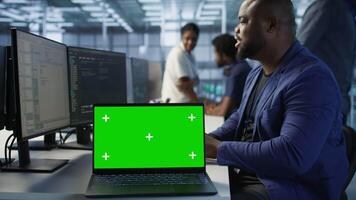 Data center technician using chroma key laptop, maintaining company network infrastructure. Server hub employee ensuring optimal system performance with isolated screen notebook, camera A video