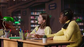 African american private teacher offering support to her students, tutoring them through a lesson plan at a library desk. Tutor providing learning materials, mentoring scholars. Camera B. video