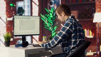 Man in home office looking at UI on PC screen, typing and executing programming code. Coding application UI used by IT developer writing and testing code in modern workspace, camera B video