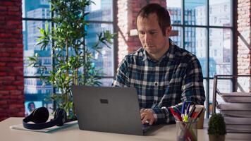 Freelancer in home office sitting at desk in front of laptop, answering phone call. Remote employee using notebook to do job online, receiving telephone call on smartphone, camera A video