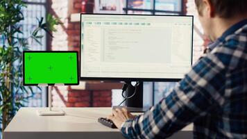 Man in home office looks at green screen tablet and computer, typing and executing programming code. Coding application used by IT developer writing and testing code using chroma key device, camera B video