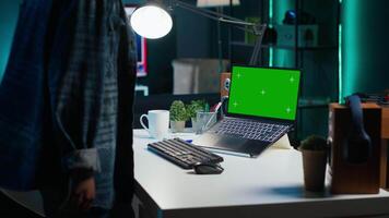 African american woman arriving in home office, sitting down at desk, typing on green screen laptop. Freelancer starting job shift, opening mockup notebook, doing email communication video
